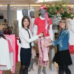 Zwei Frauen im Modegeschäft präsentieren Kleidung an Schaufensterpuppen.