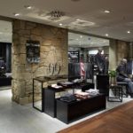 Ein Herrenmodegeschäft mit Anzügen, Hemden und Accessoires auf Tischen und Regalen.