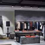 Innenansicht einer modernen Boutique mit Kleidung auf Kleiderständern und einem Tisch.