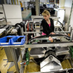Frau in einem Arbeitsumfeld, die an einer Maschinenkomponente mit Werkzeugen arbeitet.