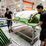 Zwei Personen arbeiten an der Montage von grünen Kunststoffteilen in einer Fabrikumgebung.