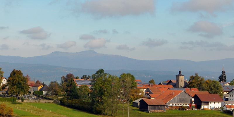 Blick auf eine ländliche Landschaft mit Dörfern und Bergen im Hintergrund unter einem bewölkten Himmel.