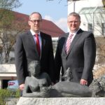 Zwei Männer in Anzügen stehen neben einer Skulptur einer liegenden Frau mit einem Vogel.
