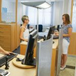 Zwei Frauen stehen am Empfang eines Büros mit Computern und Schreibtischmöbeln.