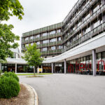 Moderne Architektur eines Gebäudes mit mehreren Etagen und großen Fenstern in einem urbanen Umfeld.