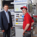 Zwei Männer stehen vor einer Steuerungseinheit in einer Fabrik für Steinbearbeitungsmaschinen.