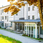 Modernes Gebäude mit Glasfront und überdachter Terrasse in Waldkirchen, umgeben von Bäumen.