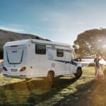 Weißes Knaus Wohnmobil mit blauen Akzenten, geparkt auf einem Feld mit einem Mann und einem Fahrrad.