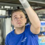 Mitarbeiter in blauer Arbeitskleidung, der einen hohen Bereich in einer Werkstatt überprüft.