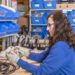 Frau mit langen, braunen Haaren, die Kabel und Stecker an einem Tisch montiert.