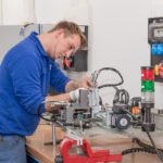 Techniker arbeitet an einer Maschine in einer Werkstatt mit verschiedenen Werkzeugen und Geräten.