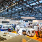 Verschiedene Wohnwagen und Wohnmobile auf einer Messe, mit Ständen und Beleuchtung im Hintergrund.
