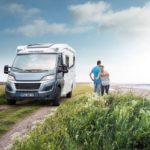 Weinsberg Wohnmobil auf einem Feldweg mit zwei Personen im Hintergrund, die auf das Wasser schauen.