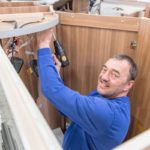 Mann mit Bohrmaschine, der in einem Wohnmobil an einer Holzverkleidung arbeitet.