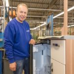 Ein Mitarbeiter steht neben einem Kühlschrank in einer Produktionsumgebung mit Werkzeugen im Hintergrund.