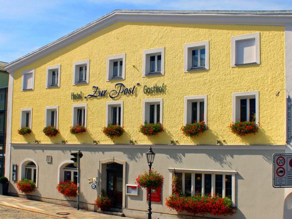Gasthaus Zur Post mit gelber Fassade und blühenden Blumenkästen an den Fenstern.