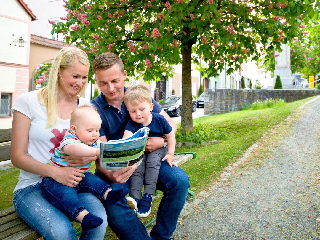 Eine Familie sitzt auf einer Bank und liest gemeinsam ein Buch im Freien.