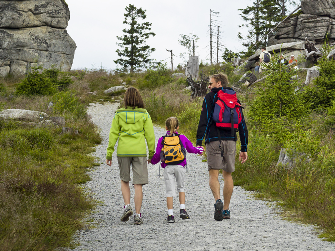 Drei Personen, darunter zwei Kinder, gehen auf einem Schotterweg in der Natur.