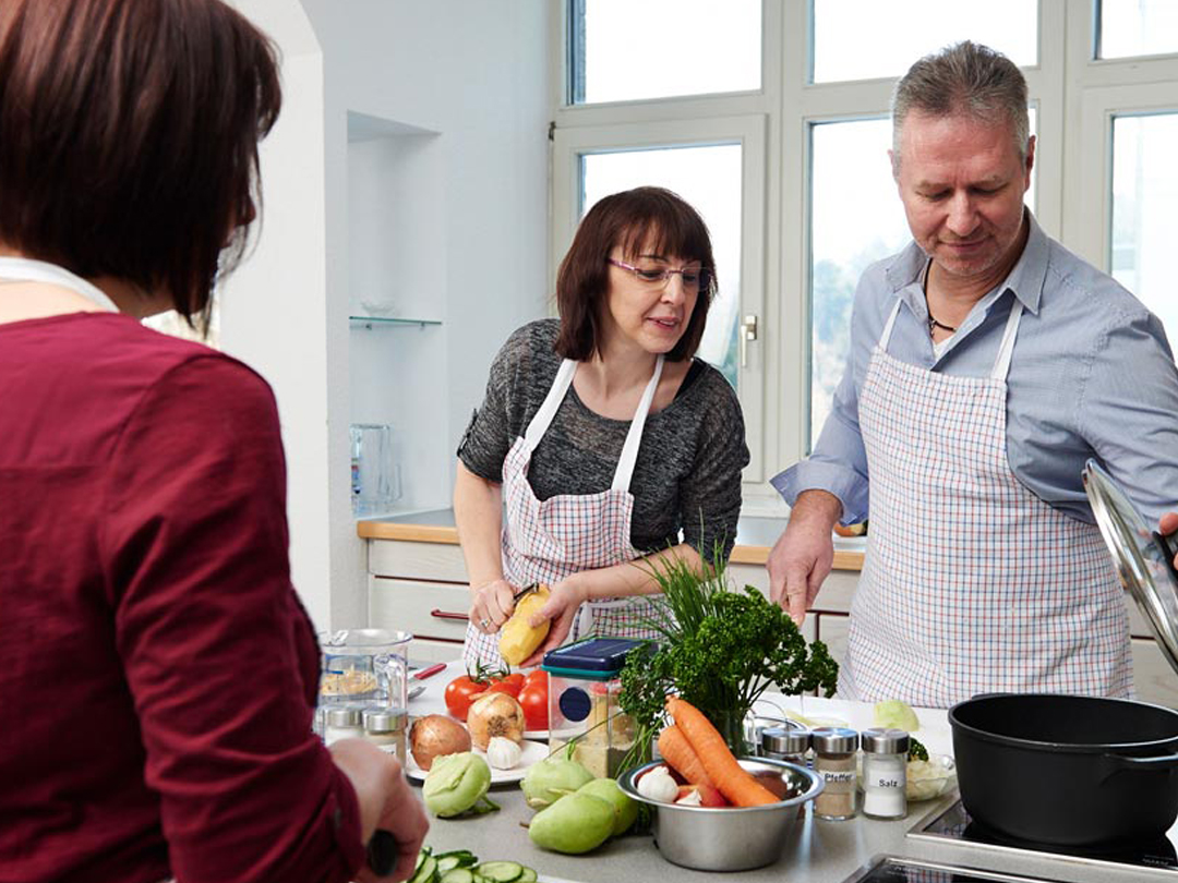 Drei Personen in einer modernen Küche bereiten gemeinsam eine Mahlzeit mit frischen Zutaten vor.