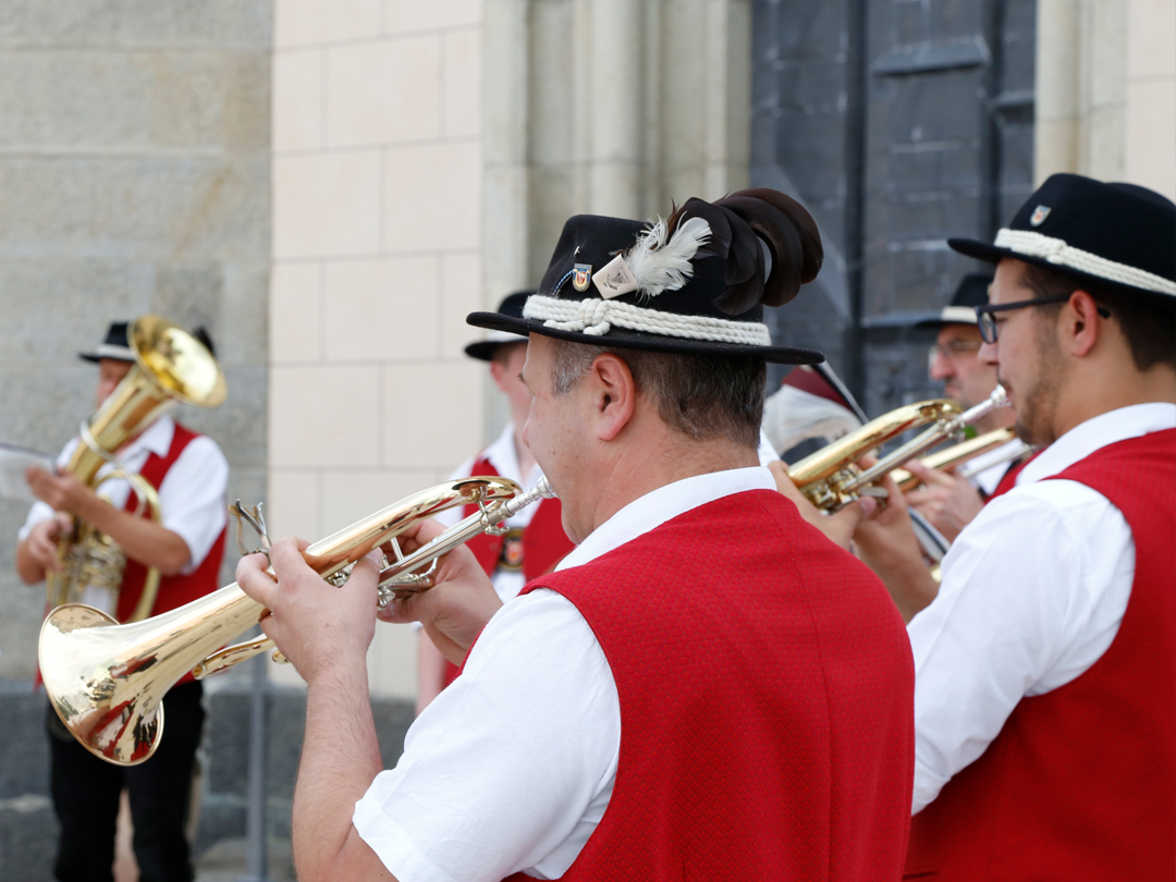 Eine Gruppe von Musikern in roten Westen spielt Trompeten und andere Blasinstrumente im Freien.