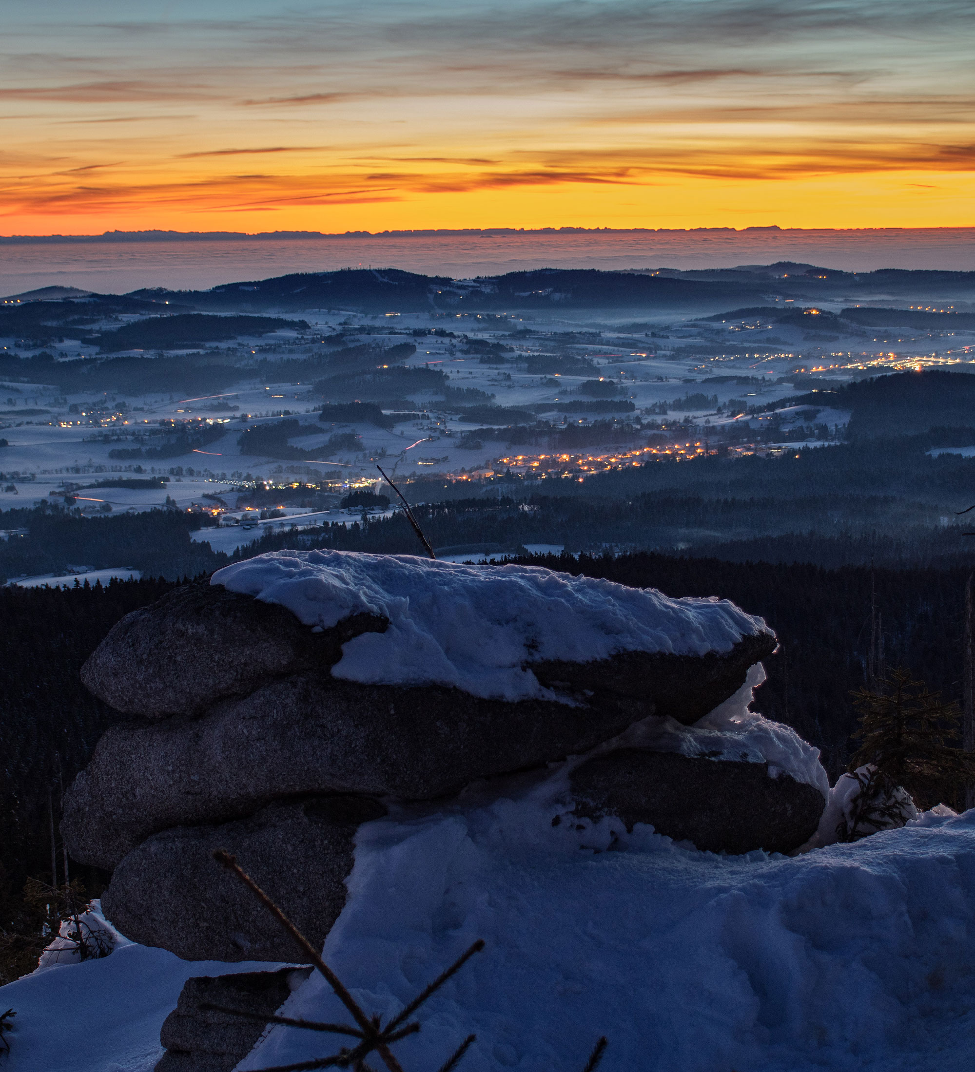 Schneebedeckter Felsen im Vordergrund mit Blick auf ein Tal bei Sonnenuntergang.
