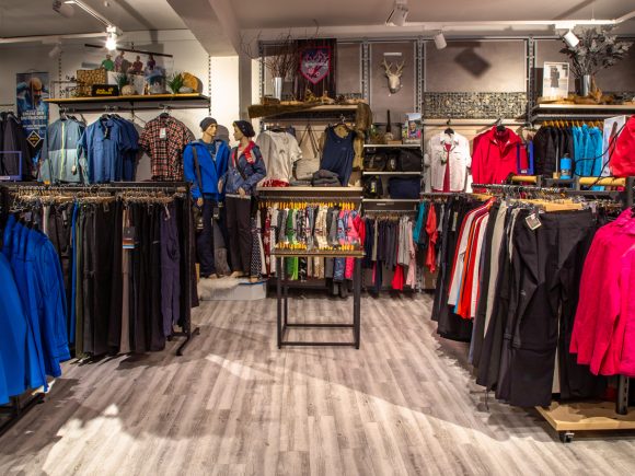 Ein Geschäft mit Sportbekleidung und Outdoor-Ausrüstung, einschließlich Jacken, Hosen und Accessoires auf Regalen.