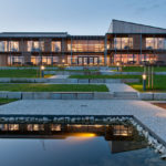 Moderne Holzarchitektur mit großen Fenstern und Gartenlandschaft bei Dämmerung.
