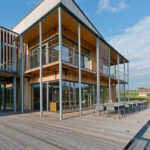 Moderne Holzarchitektur mit großen Fenstern und einer Terrasse aus Holz.