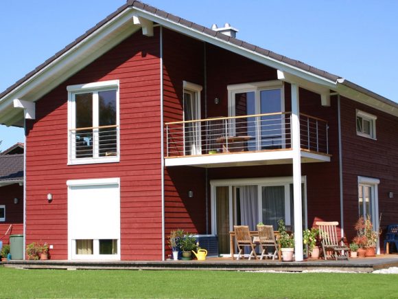 Rotes Holzhaus mit Balkon, großen Fenstern und einer Terrasse im Freien.