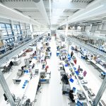 Blick auf eine moderne Produktionshalle mit mehreren Arbeitsplätzen und Mitarbeitern bei der Arbeit.