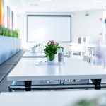 Ein Tisch mit einer Pflanze und einem Glas Wasser in einem modernen Raum mit einem Projektor im Hintergrund.