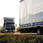 Zwei Lkw, einer in blauer Farbe und einer in hellblauer Farbe, fahren auf einer Landstraße.