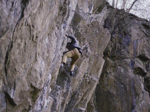 Ein Kletterer, der eine steile Felswand mit Kletterausrüstung erklimmt.