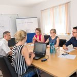 Eine Gruppe von fünf Personen sitzt um einen Tisch in einem Konferenzraum während einer Besprechung.