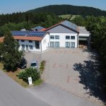 Ein modernes Gebäude mit Solarpanelen auf dem Dach und einem gepflasterten Parkplatz.