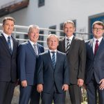 Fünf Männer in Anzügen stehen nebeneinander vor einem Gebäude.