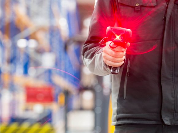 Mitarbeiter hält einen Handscanner mit rotem Laserstrahl in einem Lagerhaus.