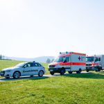 Ein Einsatzleitwagen und zwei Rettungswagen stehen auf einer Straße in einer ländlichen Umgebung.