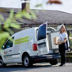 Mitarbeiterin des Roten Kreuzes steht neben einem Lieferfahrzeug mit einem Paket in der Hand.