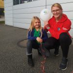 Eine Frau und ein Kind halten einen Luftballon in der Hand, beide lächeln in die Kamera.