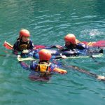 Drei Personen in Neoprenanzügen und Schwimmhelmen, die im Wasser schnorcheln.