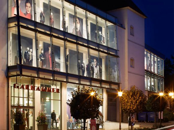 Fassade des Garhammer Modegeschäfts mit Schaufenster und beleuchteten Mannequins bei Nacht.