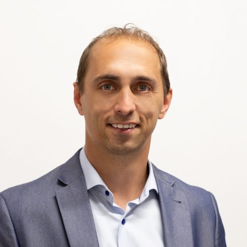 Mann mit kurzen Haaren und Anzug, der in die Kamera lächelt.