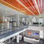 Bürointerieur mit Glaswänden, Holzdecke und moderner Beleuchtung in einem hellen Raum.