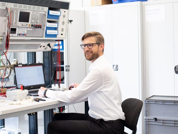 Ein Mann mit Brille sitzt an einem Tisch in einem Labor und arbeitet mit Messgeräten.