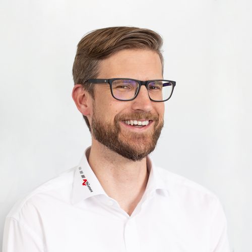 Mann mit Brille und Bart, der in einem weißen Hemd lächelt.