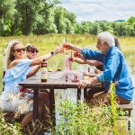 Eine Gruppe von Menschen stößt mit Getränken an einem Tisch in der Natur an.
