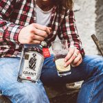 Eine Flasche Granit Bavarian Gin und ein Glas mit Getränk und Zitrone in der Hand einer Person.