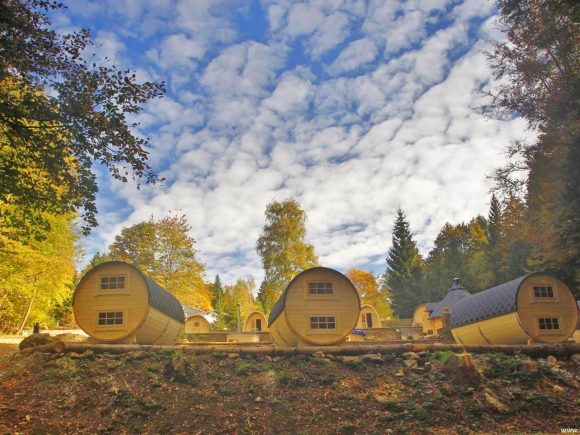 Holzhütten in Form von Fässern im Bayerischen Wald unter einem bewölkten Himmel.