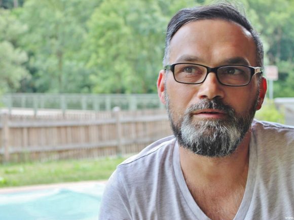 Ein Mann mit Brille und Bart, der in die Kamera schaut und lächelt.